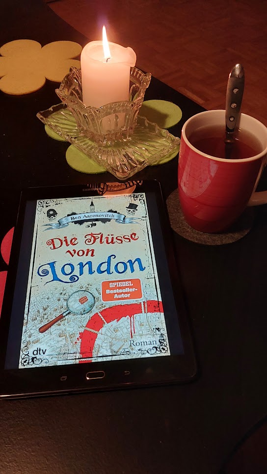 Tablet mit E-Book "Die Flüsse von London" liegt am dem Tisch neben einer Tasse Tee