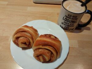 2 Franzbrötchen auf einem Teller, daneben eine Tasse Kaffee