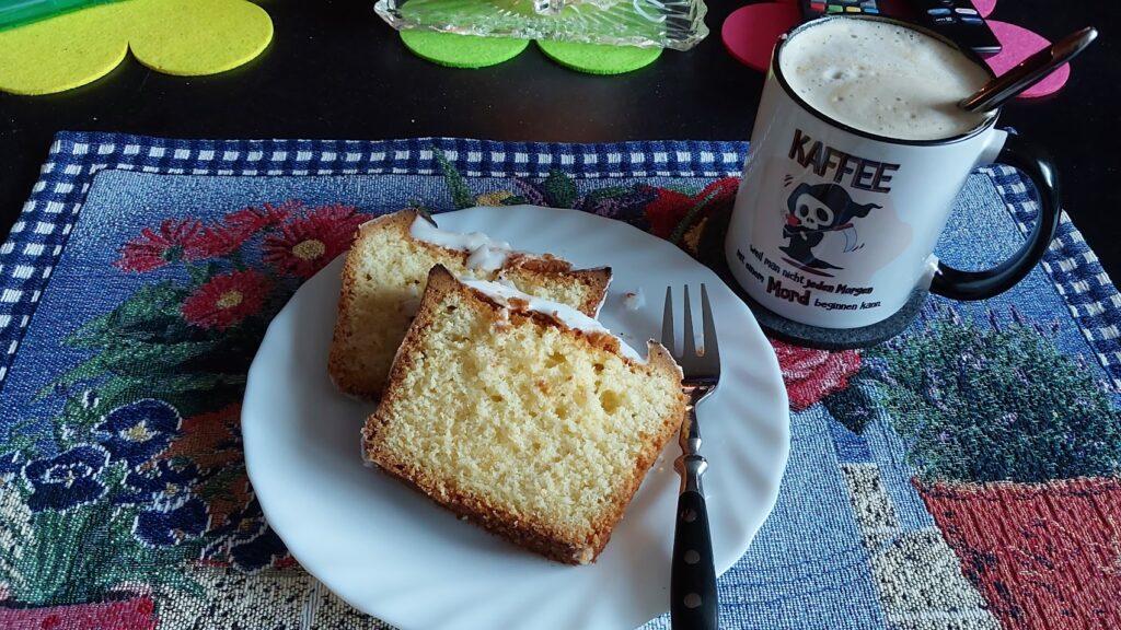 Ein Teller mit 2 Stück Zitronenkuchen. Daneben eine Tasse Kaffee.